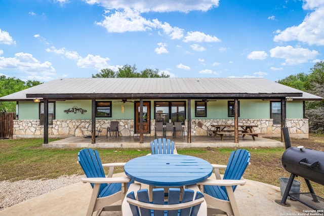 rear view of house featuring a patio, a ceiling fan, stone siding, and outdoor dining space