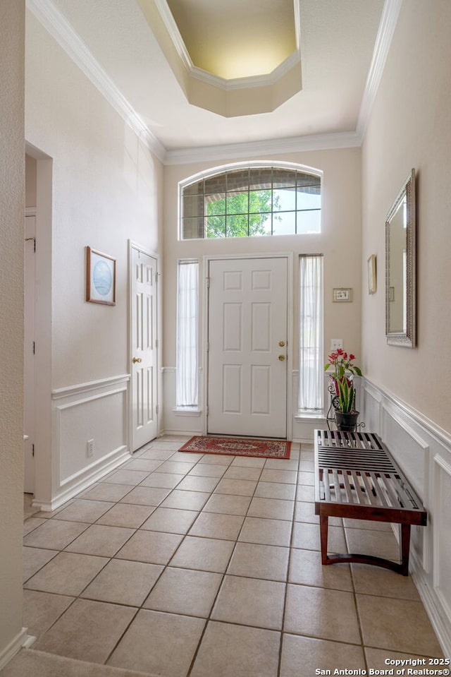 foyer entrance with a high ceiling, ornamental molding, a raised ceiling, and light tile patterned floors