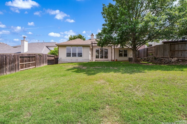 rear view of house with a fenced backyard and a yard
