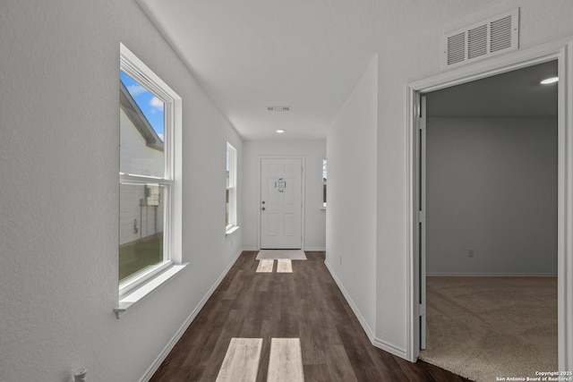 hallway with visible vents, baseboards, and dark wood-style floors