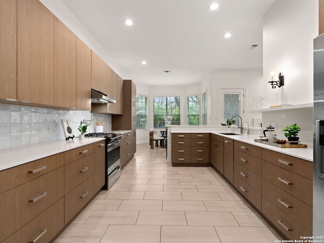 kitchen featuring a sink, gas stove, light countertops, a peninsula, and backsplash