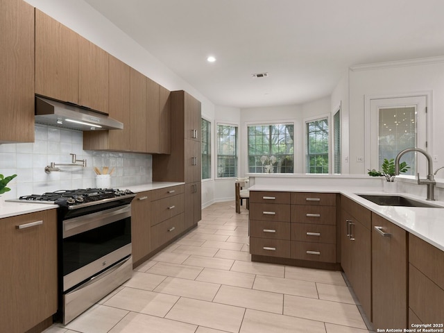 kitchen featuring a sink, stainless steel range with gas stovetop, under cabinet range hood, and light countertops