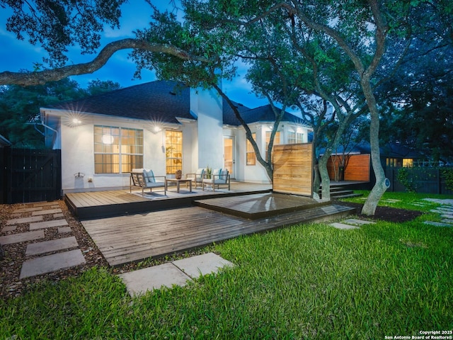 back of house with fence, stucco siding, a lawn, and a deck