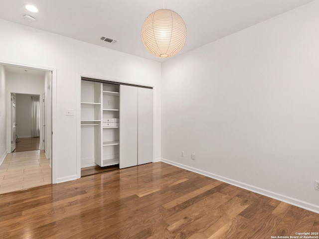 unfurnished bedroom with visible vents, baseboards, wood finished floors, and a closet