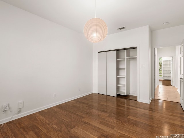 unfurnished bedroom featuring baseboards, a closet, wood finished floors, and visible vents