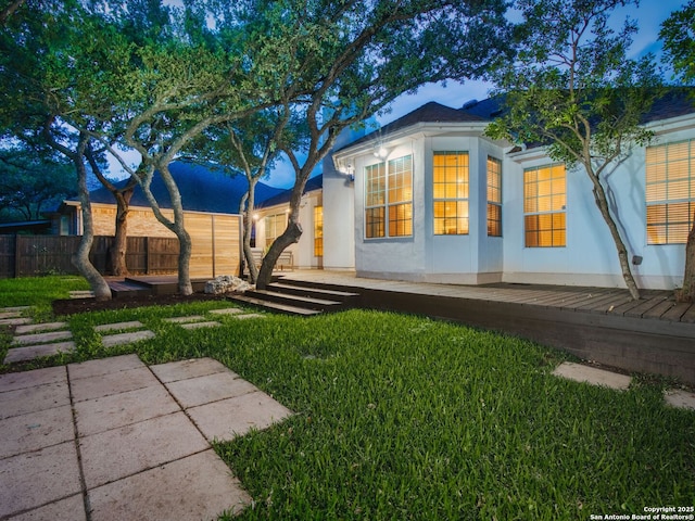 rear view of house with stucco siding, a lawn, fence, and a wooden deck