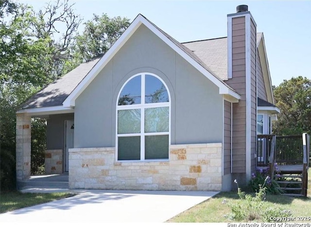 view of front of house featuring a chimney, a shingled roof, and stone siding