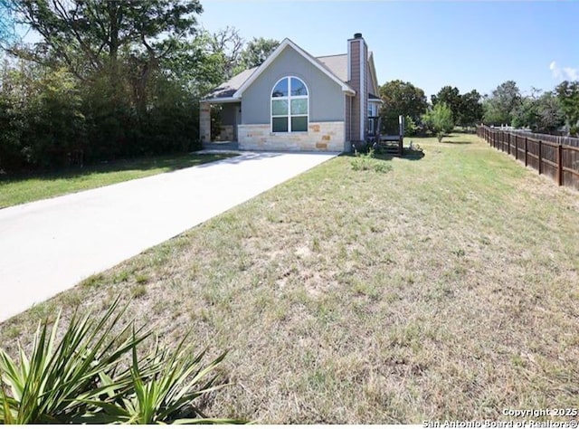 view of front facade featuring fence, stone siding, a front yard, stucco siding, and a chimney