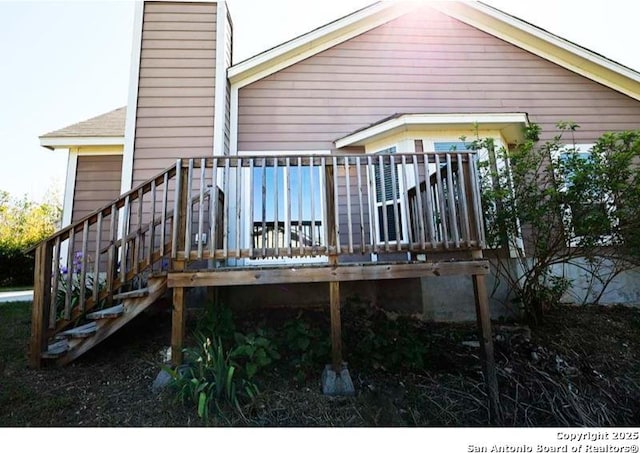 rear view of property featuring a garage, stairway, a chimney, and a deck