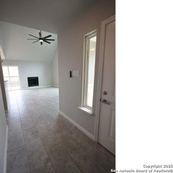 foyer entrance with a fireplace, tile patterned floors, a ceiling fan, baseboards, and lofted ceiling