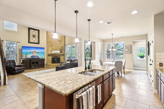 kitchen with visible vents, light tile patterned flooring, light stone countertops, a stone fireplace, and a sink