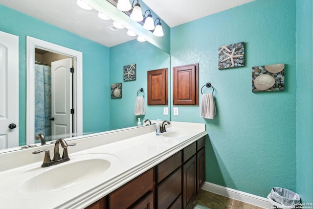 full bath with double vanity, a sink, a textured wall, and baseboards