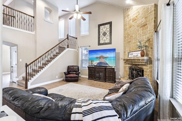 living area with a ceiling fan, a stone fireplace, stairway, high vaulted ceiling, and baseboards