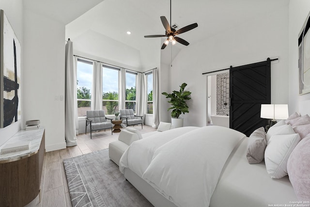 bedroom with a barn door, light wood-style floors, a ceiling fan, baseboards, and vaulted ceiling