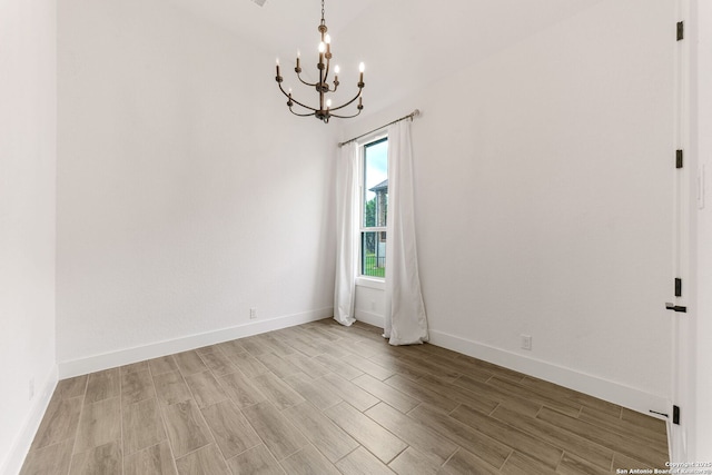 empty room featuring an inviting chandelier, baseboards, and light wood-style floors