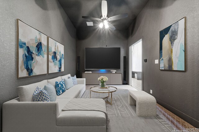 living room featuring a ceiling fan, a textured wall, and a high ceiling