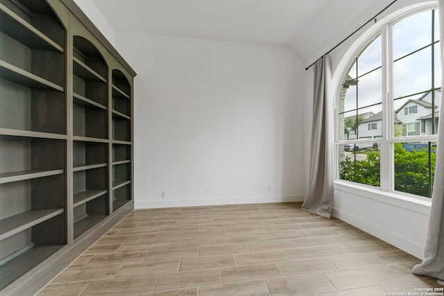 spare room with baseboards, lofted ceiling, and light wood-style floors