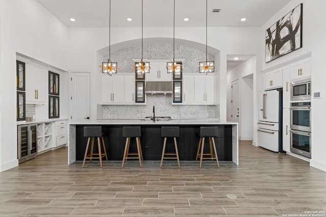 kitchen featuring wine cooler, under cabinet range hood, a notable chandelier, and stainless steel appliances