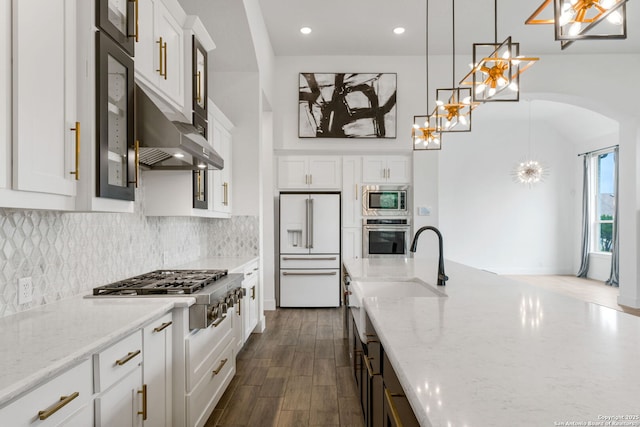 kitchen featuring a sink, light stone countertops, under cabinet range hood, arched walkways, and stainless steel appliances