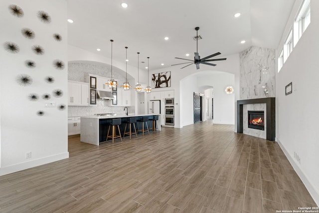 unfurnished living room with a ceiling fan, wood finished floors, high vaulted ceiling, recessed lighting, and a premium fireplace