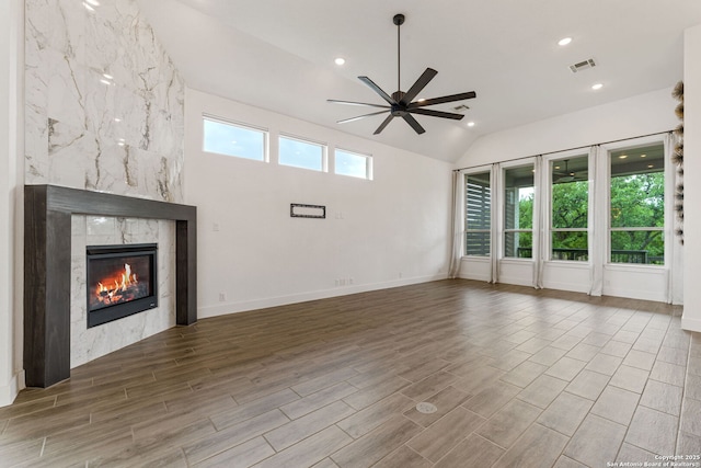 unfurnished living room with a ceiling fan, visible vents, vaulted ceiling, a tile fireplace, and wood finished floors