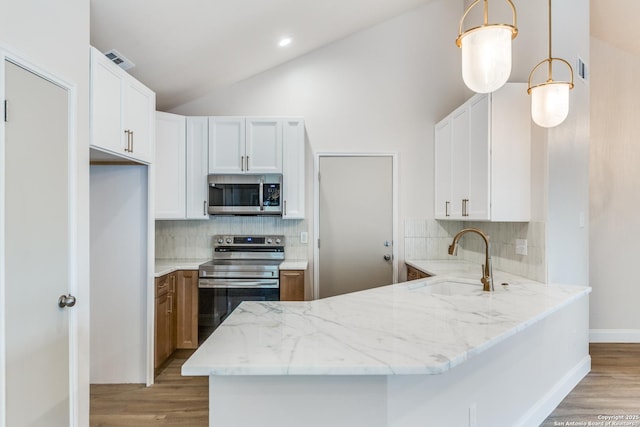 kitchen featuring light stone countertops, a sink, a peninsula, lofted ceiling, and stainless steel appliances