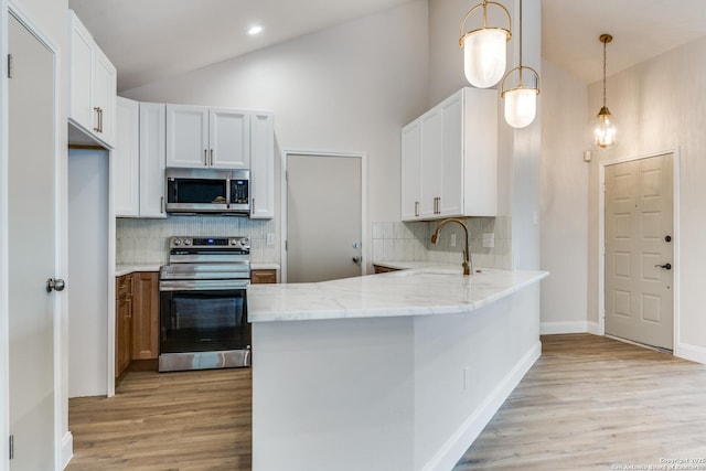 kitchen featuring a peninsula, light wood-style floors, light stone counters, appliances with stainless steel finishes, and backsplash