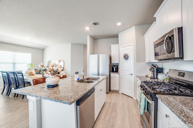 kitchen with appliances with stainless steel finishes, a center island with sink, a sink, white cabinets, and light wood-style flooring