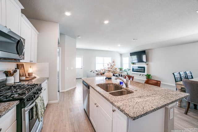 kitchen featuring light stone countertops, open floor plan, a center island with sink, a sink, and appliances with stainless steel finishes