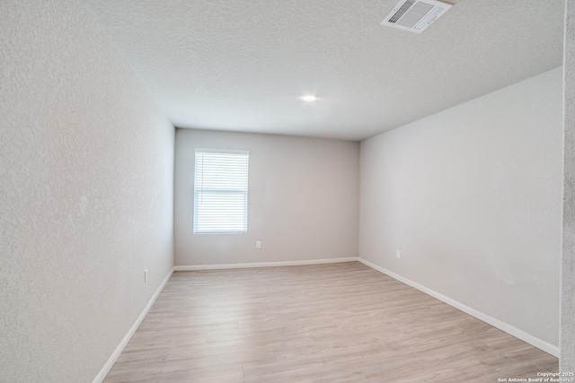 unfurnished room with baseboards, a textured ceiling, light wood-style flooring, and visible vents
