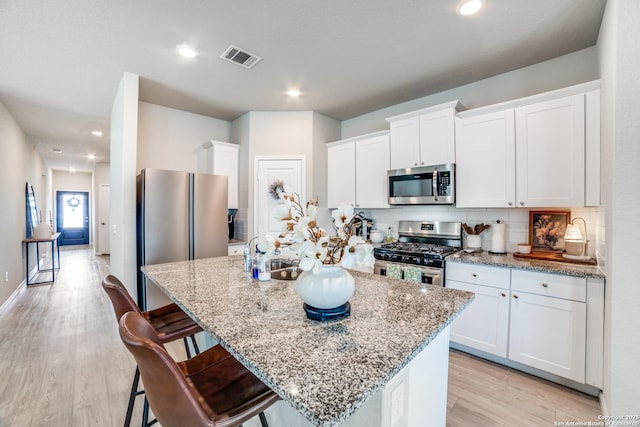 kitchen featuring appliances with stainless steel finishes, an island with sink, light wood-style flooring, and visible vents