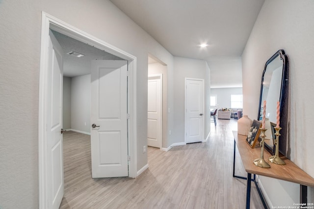 hallway with baseboards, light wood finished floors, and visible vents