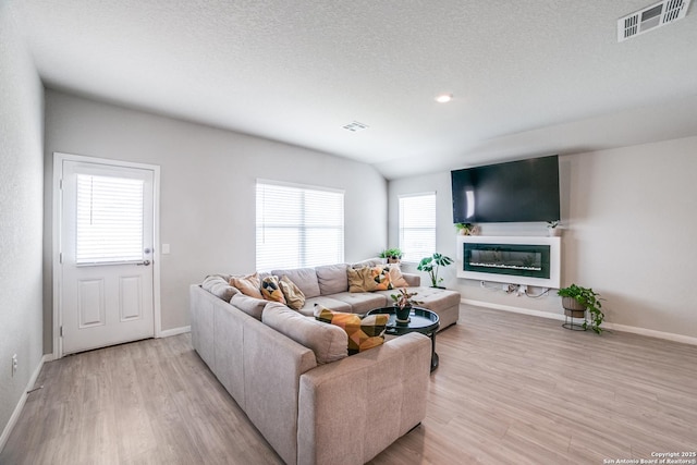 living room featuring a glass covered fireplace, baseboards, light wood finished floors, and visible vents