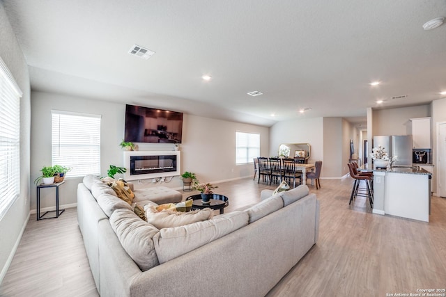 living room with light wood-style floors, baseboards, a glass covered fireplace, and visible vents