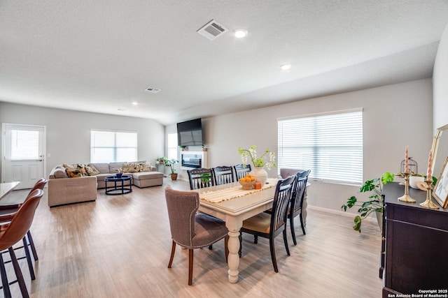 dining area featuring a glass covered fireplace, baseboards, light wood-type flooring, and visible vents