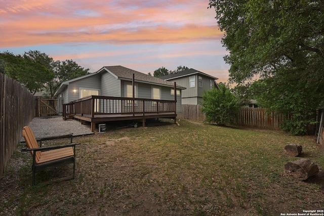 back of property at dusk featuring a fenced backyard, a yard, and a deck
