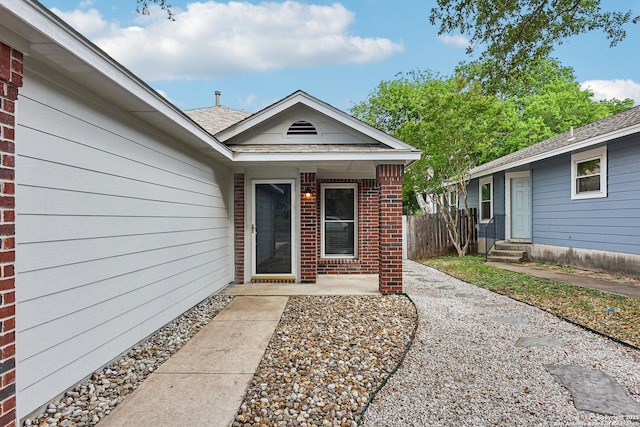 view of exterior entry featuring brick siding and fence