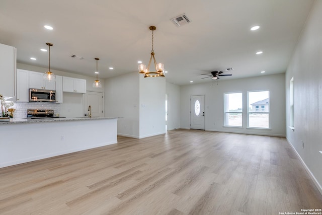 unfurnished living room with a sink, light wood-style flooring, ceiling fan with notable chandelier, recessed lighting, and visible vents