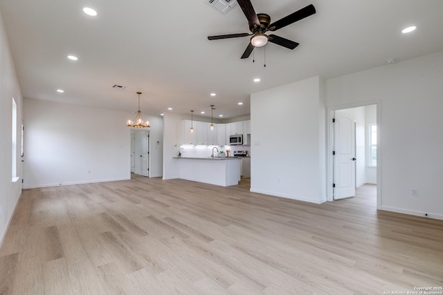 unfurnished living room with a sink, baseboards, ceiling fan with notable chandelier, light wood-style floors, and recessed lighting