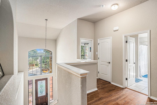hall featuring a textured wall, an inviting chandelier, a textured ceiling, wood finished floors, and lofted ceiling