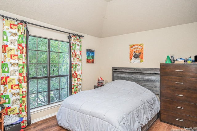 bedroom with vaulted ceiling, multiple windows, and wood finished floors