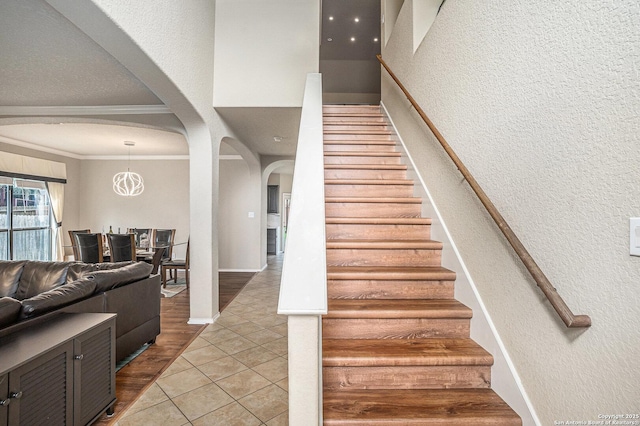 staircase with crown molding, arched walkways, a textured wall, and tile patterned floors