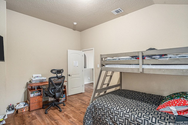 bedroom featuring visible vents, a textured ceiling, lofted ceiling, and wood finished floors