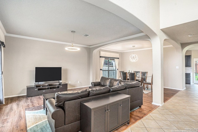 living area with arched walkways, baseboards, visible vents, and ornamental molding