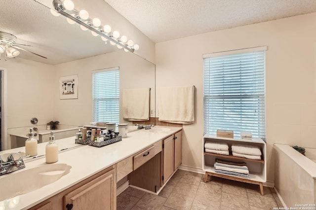 full bath with double vanity, a ceiling fan, a sink, and a textured ceiling