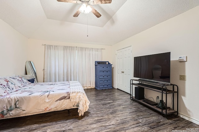 bedroom with a ceiling fan, a tray ceiling, and dark wood-style flooring