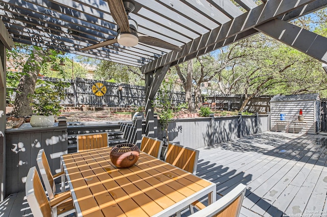 wooden terrace featuring a pergola, ceiling fan, a shed, a fenced backyard, and outdoor dining area