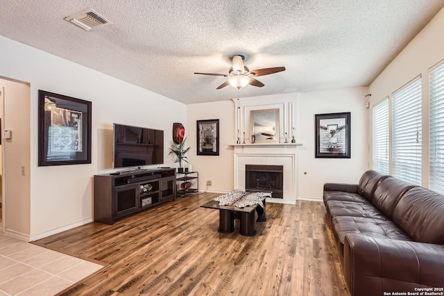 living area with ceiling fan, a fireplace, a textured ceiling, wood finished floors, and visible vents