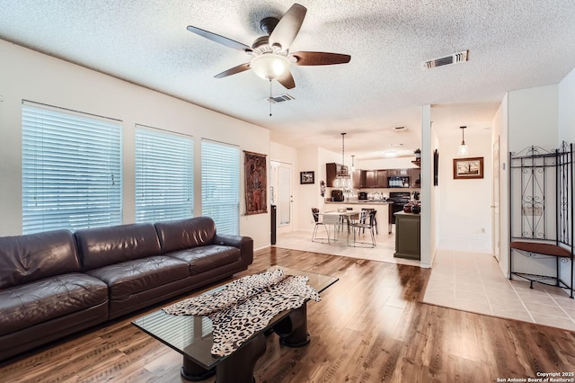 living area with a ceiling fan, light wood finished floors, and visible vents