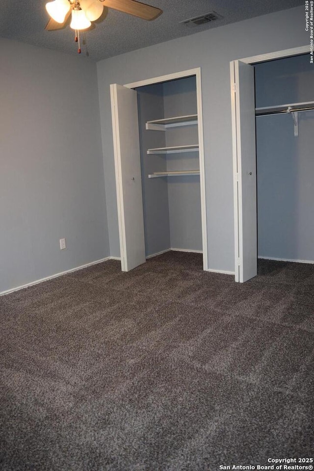 unfurnished bedroom featuring carpet floors, a ceiling fan, multiple closets, and visible vents